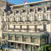 Ornate European-style luxury hotel on a palm-lined seaside street with iron balconies and intricate stonework.