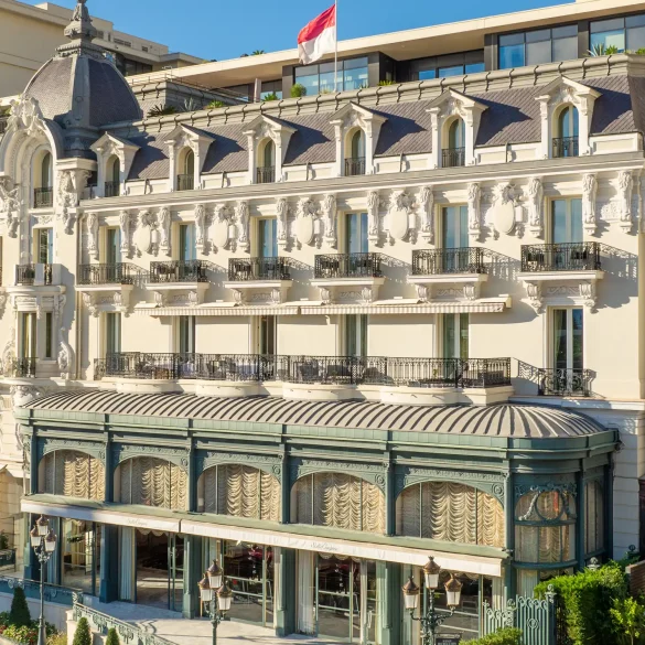 Ornate European-style luxury hotel on a palm-lined seaside street with iron balconies and intricate stonework.