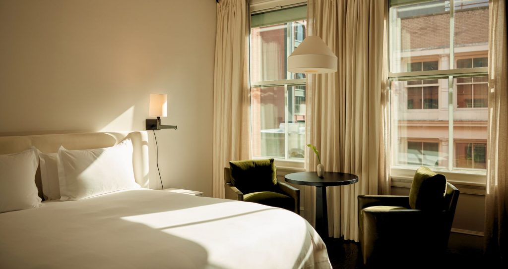 Chambre du Mercer Hotel après rénovation 2026 : parquet en bois, rideaux en lin, palette de verts doux et touches de cuir