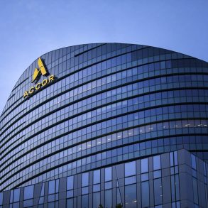 Curved glass office building with ACCOR logo on the facade against a blue sky.
