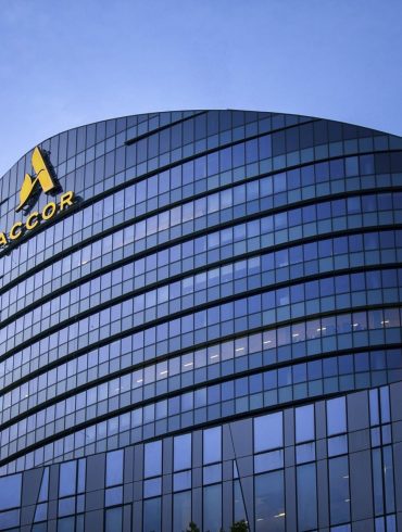 Curved glass office building with ACCOR logo on the facade against a blue sky.