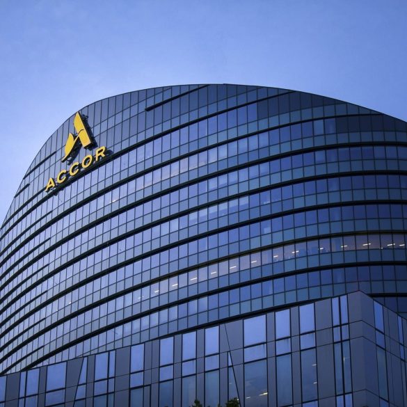 Curved glass office building with ACCOR logo on the facade against a blue sky.