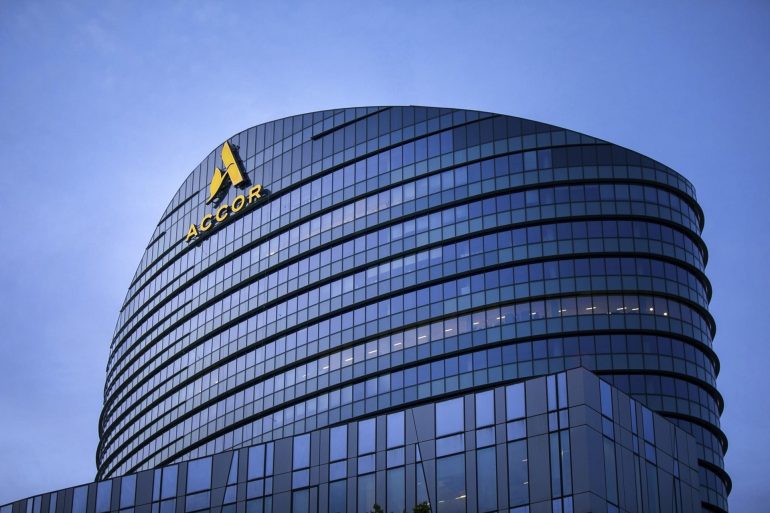 Curved glass office building with ACCOR logo on the facade against a blue sky.