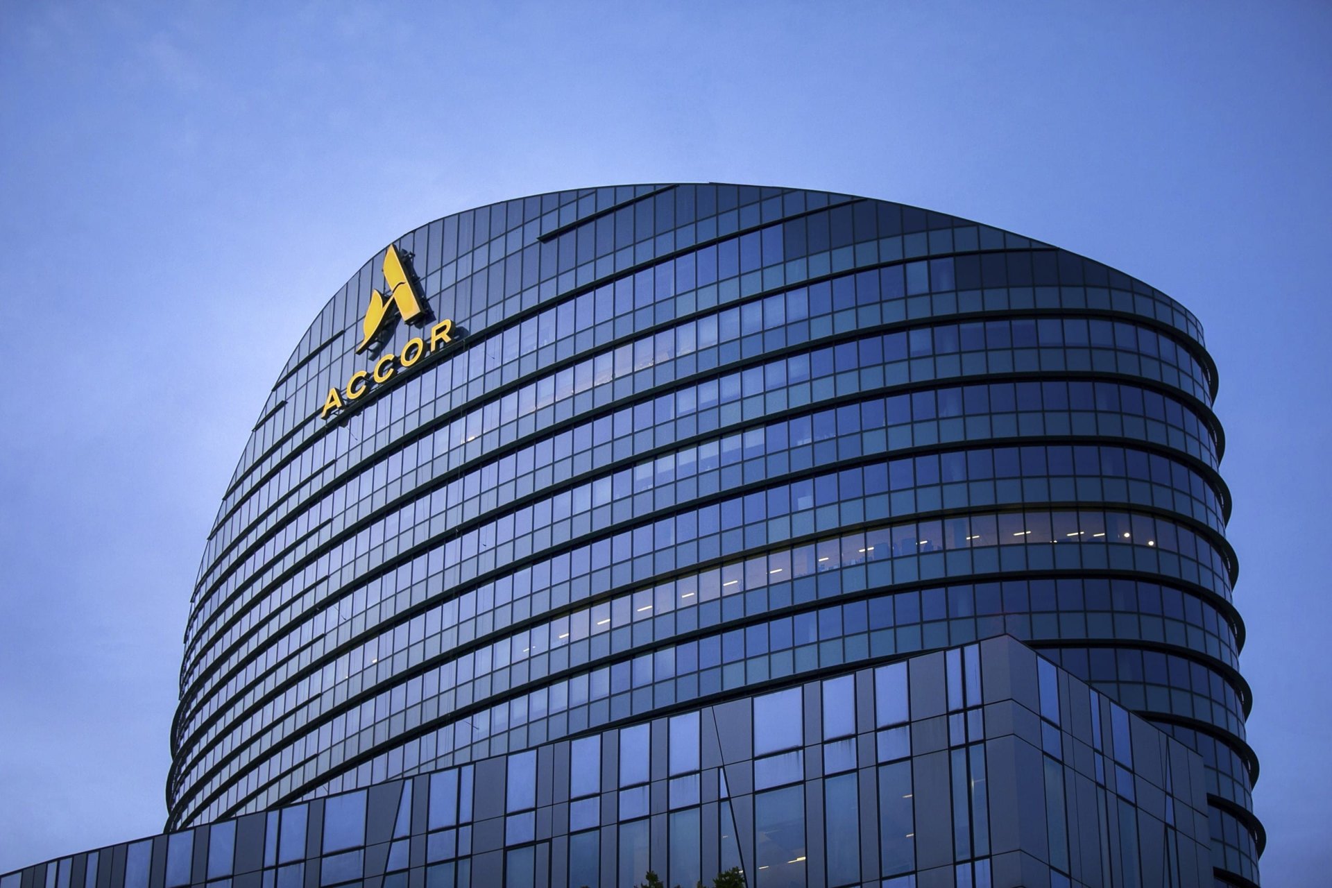 Curved glass office building with ACCOR logo on the facade against a blue sky.