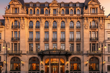 Ornate historic hotel facade at sunset with arched ground-floor windows and ornate detailing above, warm entrance lights glowing.
