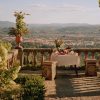 Table set for a meal on a stone terrace with potted plants and a view of a valley and distant hills