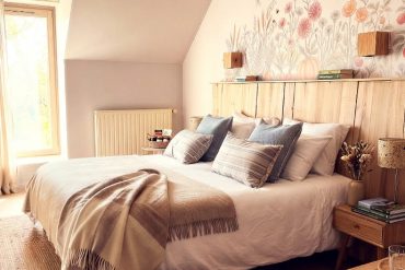 Cozy bedroom with a white duvet, beige throw, and decorative pillows on a wooden bed beneath a pastel floral mural above the headboard.