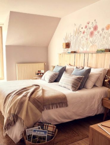Cozy bedroom with a white duvet, beige throw, and decorative pillows on a wooden bed beneath a pastel floral mural above the headboard.