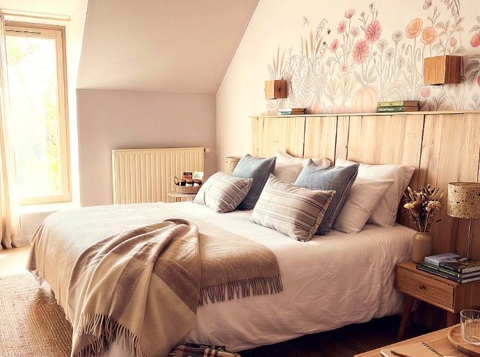 Cozy bedroom with a white duvet, beige throw, and decorative pillows on a wooden bed beneath a pastel floral mural above the headboard.