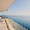 Modern balcony overlooking the ocean with glass railing and blue‑striped lounge chairs along a tiled terrace.