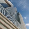 Low-angle view of tall glass skyscrapers with horizontal louvers against a clear blue sky, emphasizing their geometric lines and modern architecture.