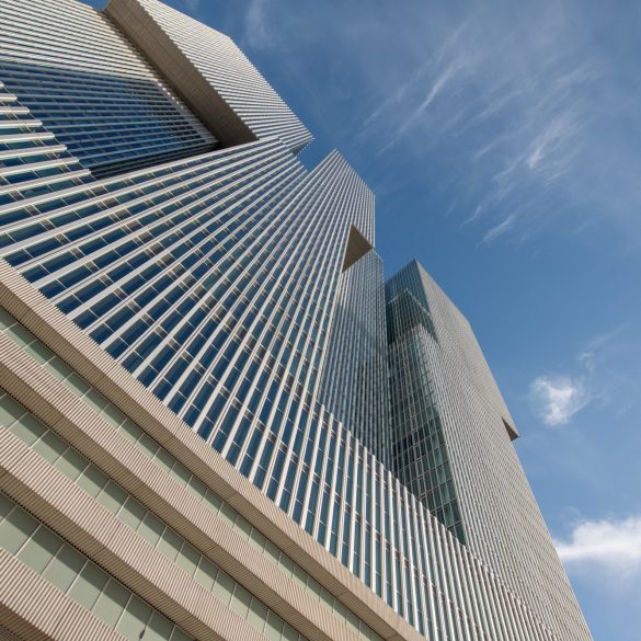 Low-angle view of tall glass skyscrapers with horizontal louvers against a clear blue sky, emphasizing their geometric lines and modern architecture.