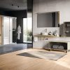 Modern bathroom showroom with grey textured wall, gold faucet, wall mirror, and floating countertop against light wood flooring.