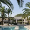 Luxurious outdoor resort pool area with palm trees, white lounge chairs, and umbrellas beside a modern villa.