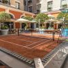 Outdoor courtyard with a small clay tennis court, surrounded by orange walls, white arches, and potted trees.