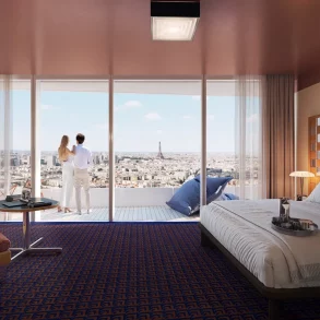 Couple stands on a balcony in a modern hotel room, overlooking a city skyline with the Eiffel Tower in the distance.