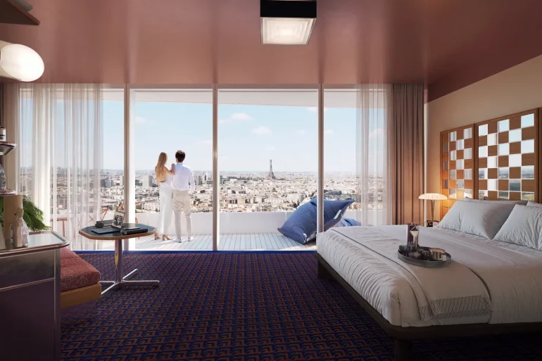 Couple stands on a balcony in a modern hotel room, overlooking a city skyline with the Eiffel Tower in the distance.