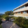 Modern wooden-and-stone house with large glass windows, poolside terrace, and landscaped garden under a blue sky.
