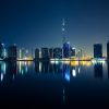 Night city skyline with illuminated skyscrapers reflecting on calm water.