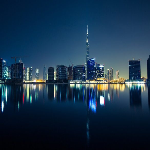 Night city skyline with illuminated skyscrapers reflecting on calm water.