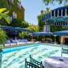 Poolside scene with turquoise water, white loungers under blue canopies and ivy-covered walls in a sunny resort setting.