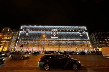 Le 103-111 Champs-Élysées habillé d’une malle Louis Vuitton géante illuminée, la nuit, sur l’avenue.