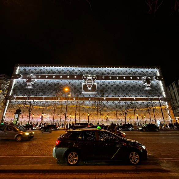 Le 103-111 Champs-Élysées habillé d’une malle Louis Vuitton géante illuminée, la nuit, sur l’avenue.