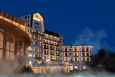 L'Hôtel Royal de l'Évian Resort illuminé la nuit au-dessus de son parcours thermal, au bord du lac Léman