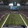 A packed football stadium with a massive video screen hanging over the field showing players, and the Cowboys end zone visible at the near end of the field.