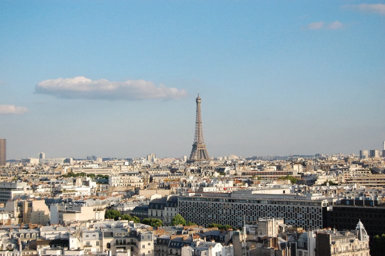 Paris skyline with the Eiffel Tower rising above white rooftops under a clear blue sky, daytime view.