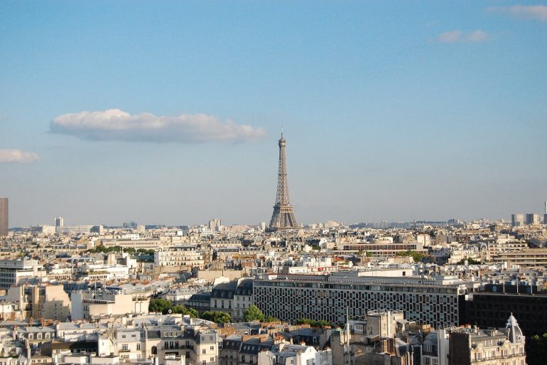 Paris skyline with the Eiffel Tower rising above white rooftops under a clear blue sky, daytime view.