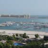 Harbor filled with boats at Dubai Marina, high-rise apartments along the shore, with the Burj Al Arab visible in the distance under a clear blue sky.