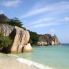 Tropical beach with large smooth granite boulders along the shoreline, turquoise sea and blue sky with wispy clouds.