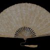 Ivory lace hand fan fully opened in a semicircle, showing intricate floral patterns and a tassel at the handle against a black background.