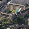 Aerial view of a historic city block with a central courtyard, blue rooftop pool, and manicured gardens.