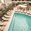 Aerial view of a hotel rooftop pool deck with green cushioned loungers, umbrellas, and seating, overlooking the sea.