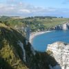 Cliff-top church and grassy fields overlook a blue sea and sandy cove below.