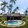 Tropical resort scene with thatched-roof huts, lush palm trees, and a central pool under a blue sky.