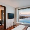 Modern hotel room with a freestanding tub by a large window overlooking water and cityscape beyond.