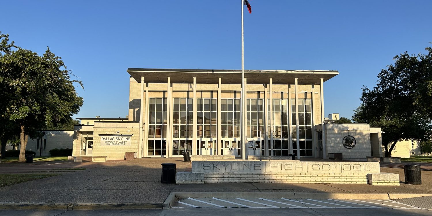 Dallas Skyline High School facade with a tall flagpole and flags against a clear blue sky.