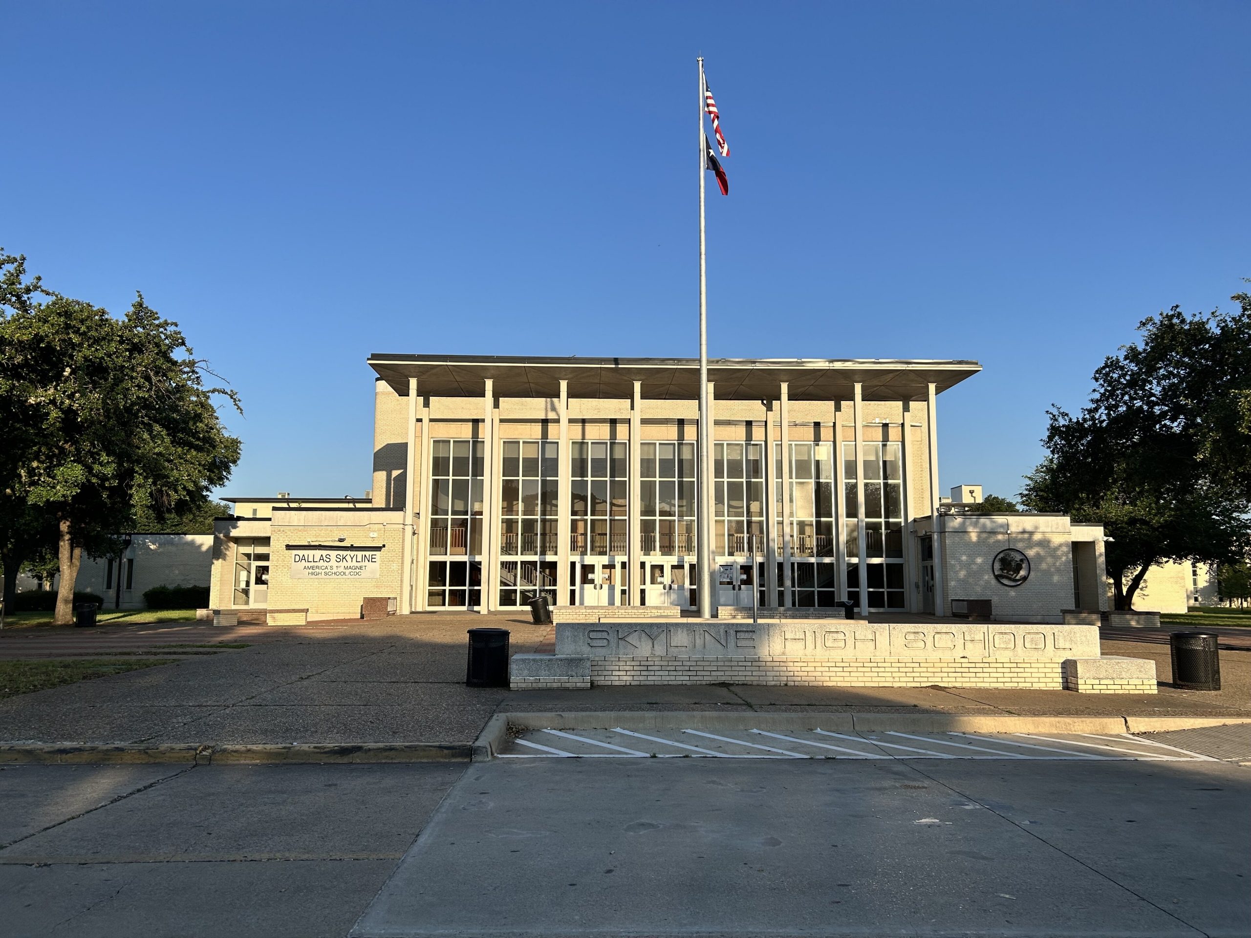 Dallas Skyline High School facade with a tall flagpole and flags against a clear blue sky.