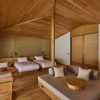 Wood-clad hotel suite with two low platform beds, a sofa area, and a round coffee table in warm lighting