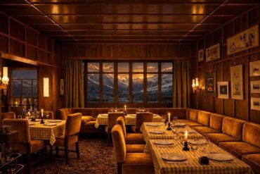 Cozy alpine restaurant with wooden walls, candlelit tables, and a window showing snow-capped mountains at sunset.