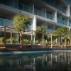 Modern hotel with glass balconies and a wooden poolside cabana lounge along a reflective pool in front of the building.