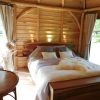 Cozy rustic bedroom in a wooden cabin with a large bed, soft pillows, and warm lighting by the headboard window.