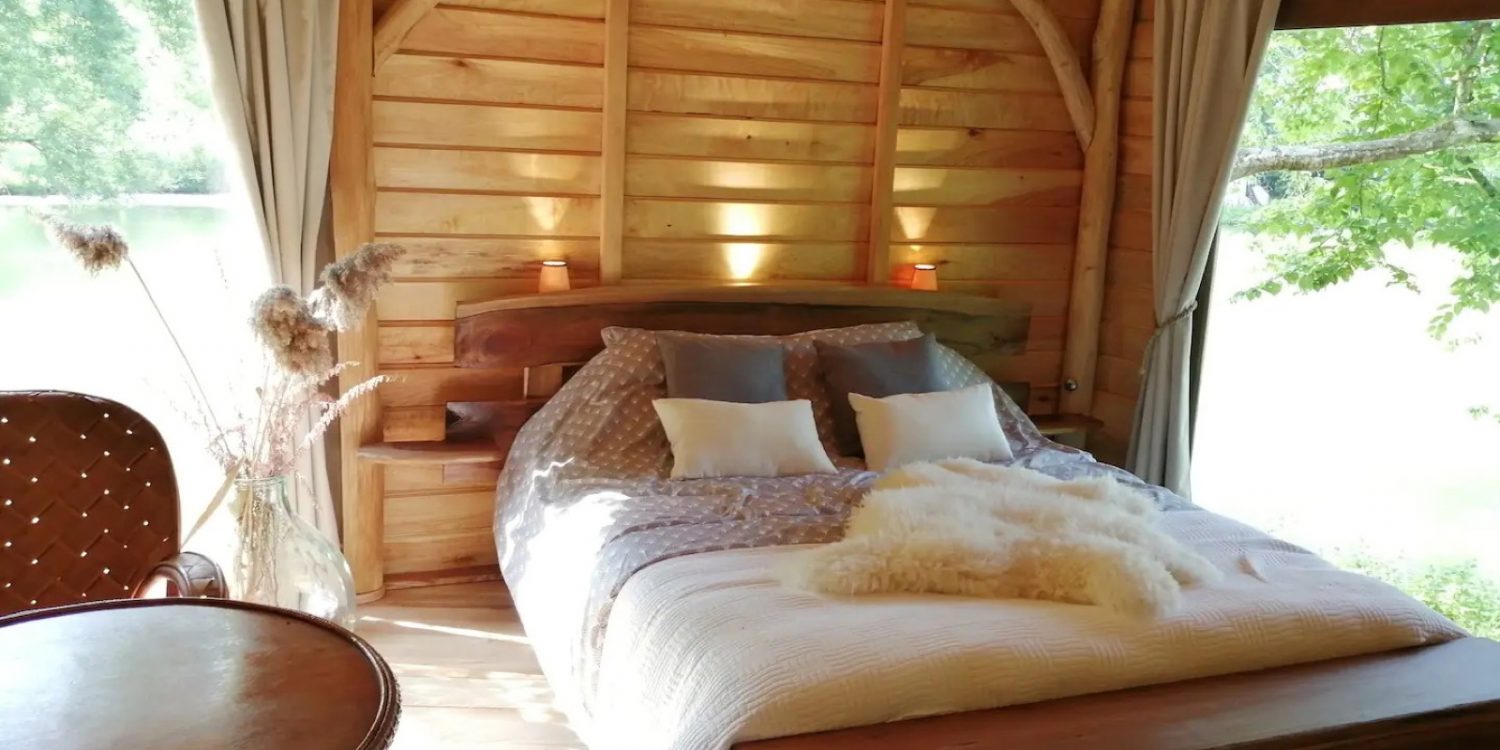 Cozy rustic bedroom in a wooden cabin with a large bed, soft pillows, and warm lighting by the headboard window.