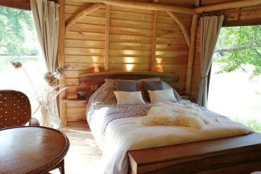 Cozy rustic bedroom in a wooden cabin with a large bed, soft pillows, and warm lighting by the headboard window.