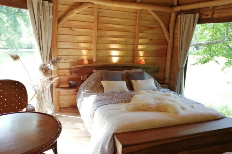 Cozy rustic bedroom in a wooden cabin with a large bed, soft pillows, and warm lighting by the headboard window.