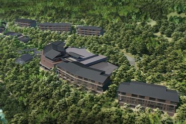 Modern hillside resort with dark-roofed lodges nestled among dense trees and winding paths on a forested slope