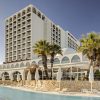 Exterior view of Crowne Plaza hotel with a pool area, white arched architecture, and palm trees in the foreground.